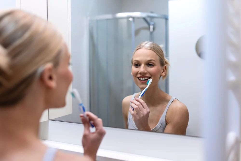 Smiling young woman looking in the mirror as she brushes her teeth